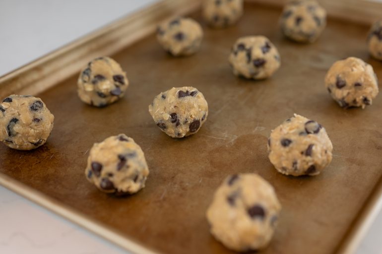 Close up of raw cookies rolled into balls on a cookie sheet.