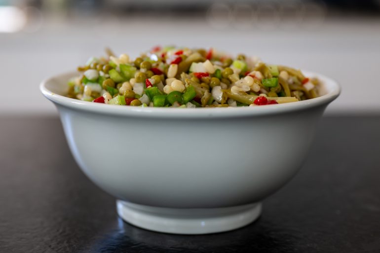 Marinated vegetable salad in white bowl on a black counter top.