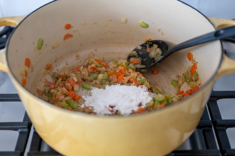 Flour added to a pot of vegetables on a stove.