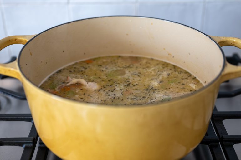 Chicken simmering in a pot on a stove in a yellow pot.