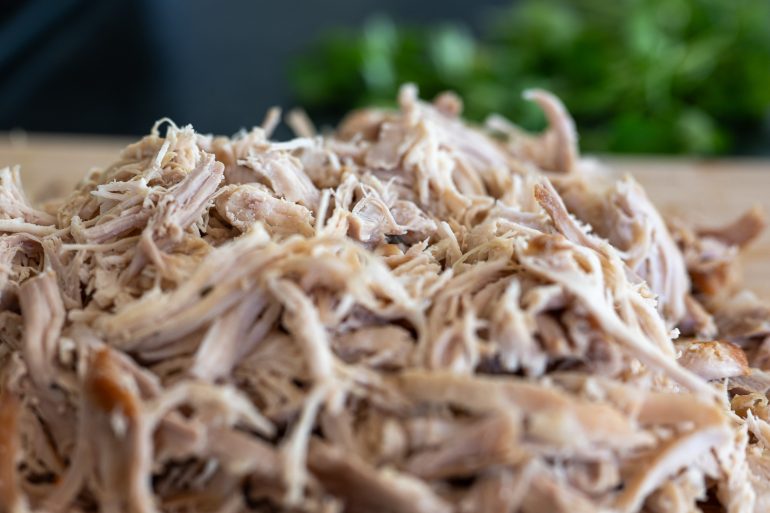 Shredded chicken thighs on a cutting board.