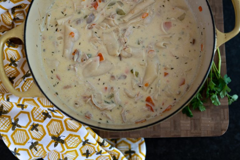 A big pot of chicken and dumplings. The photo is taken from above. The pot is sitting on a cutting board and there is a tea bowl to the side.