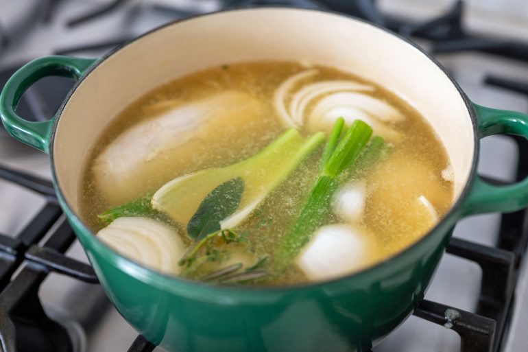 A green pot with onion, celery, bay leaf, and chicken breast.