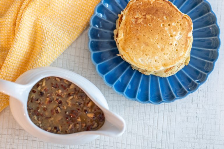 Overhead view of golden pancakes on a blue plate with a gravy boat of pecan praline sauce.