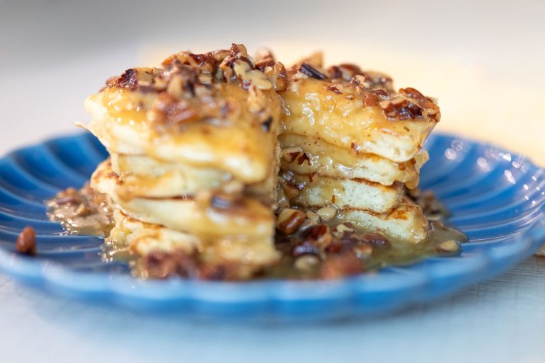 Stack of buttermilk pancakes on a blue plate topped with a warm pecan praline sauce.