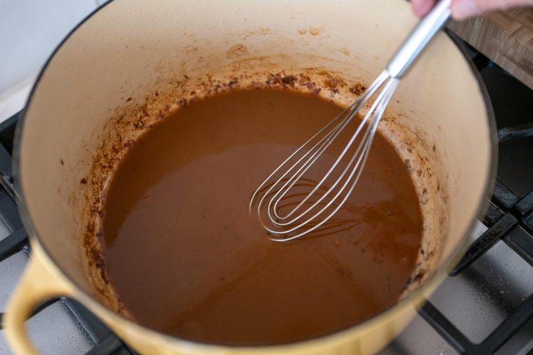 A shot from above of a heavy pot. You can see a roux whisk mixing a dark brown roux inside the pot.