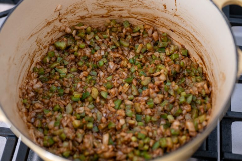 A shot from above of a dutch oven that contains a dark roux and a mixture of vegetables. There is diced celery, green pepper, and onion in the pot.