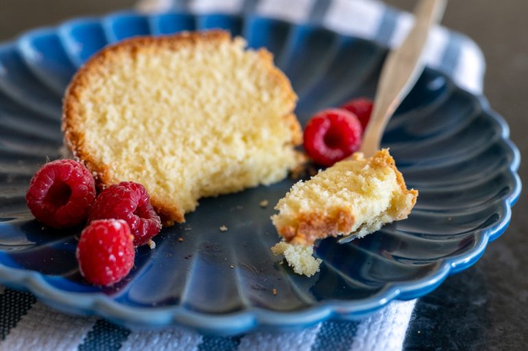 A close up of a piece of cake on a blue plate. A fork has cut a piece of cake from the cake and it in the foreground.
