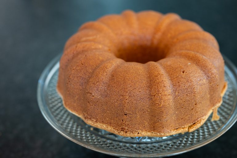 An entire classic cream cheese pound cake is shot from slightly above and to the side. It is a beautiful golden brown.