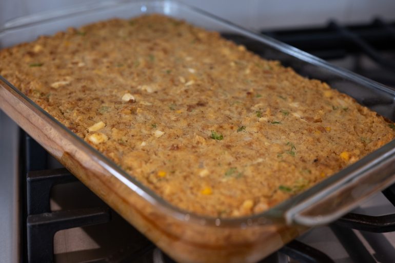 A 9 by 13 inch baking dish with baked cornbread dressing. The top is golden brown and you can see chunks of egg and celery.