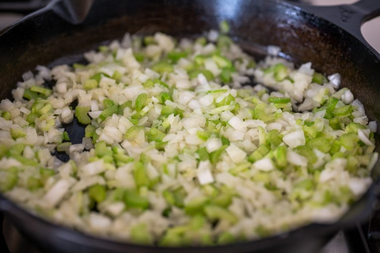 Onion and celery sautéing in an iron skillet.