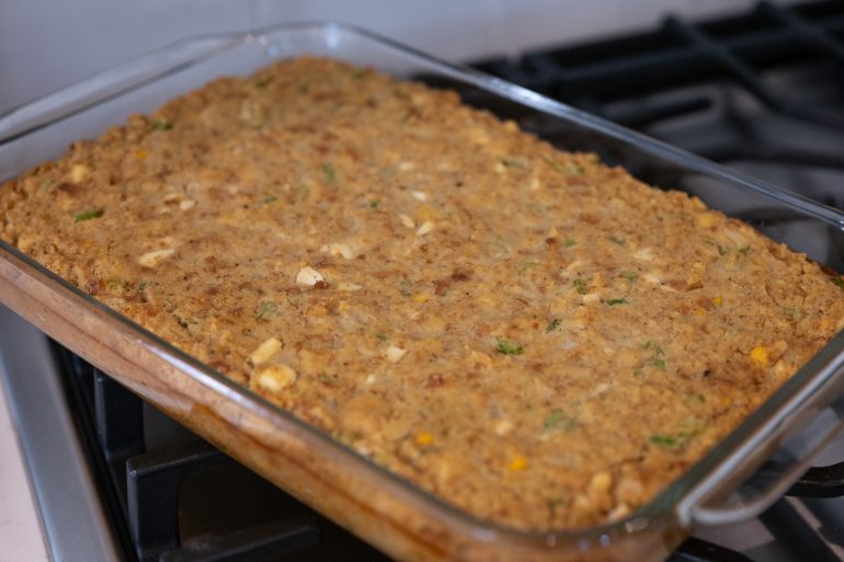 Cornbread dressing in a 9x13 inch baking dish. The top is golden brown and you can see small pieces of egg and celery.