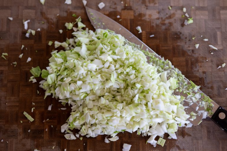 Close up of some chopped cabbage on a cutting board with a knife.