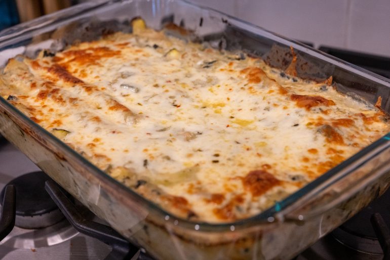 a baking dish filled with creamy vegetarian enchiladas verdes. The top of the enchiladas is cheesy and golden brown.