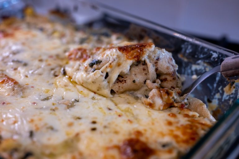 a baking dish with creamy vegetarian enchiladas verdes. A spatula is lifting out an enchilada that looks hot and cheesy.