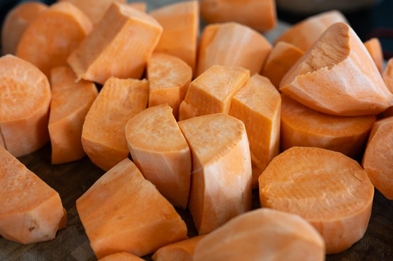 Sweet potatoes in a jumbled pile which have been peeled and cut into medium sized pieces.