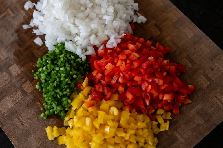Chopped bell peppers and jalapeno and onion on a cutting board. 