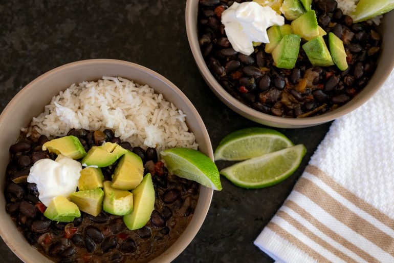 Two bowls of black bean soup on a black countertop in a beige bowl. 