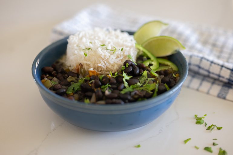 Bowl of Cuban black bean soup in a blue bowl, There is rice in the bowl and it is sprinkled with cilantro and jalapeno. 