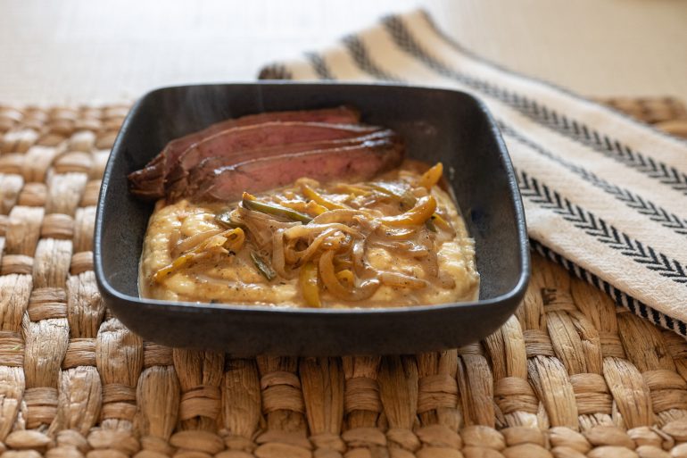 side view of creole flank steak over cheddar grits with creamy pan sauce.