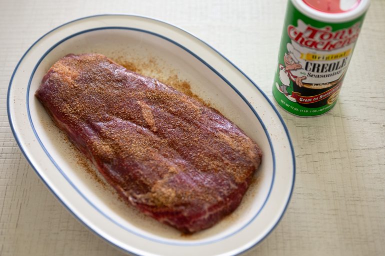 A raw flank steak coated in creole seasoning on a blue and white platter. 