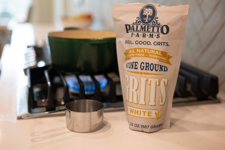 A bag of palmetto farms stone ground grits. The focus is on the bag but you can see a measuring cup and a pot on a stove with a burner in the background. 