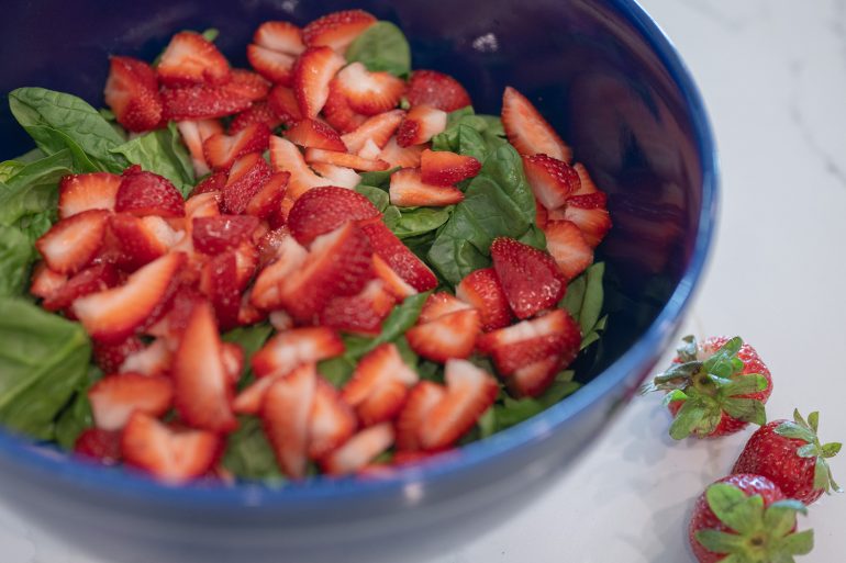 A large blue bowl containing spinach and sliced strawberries. 