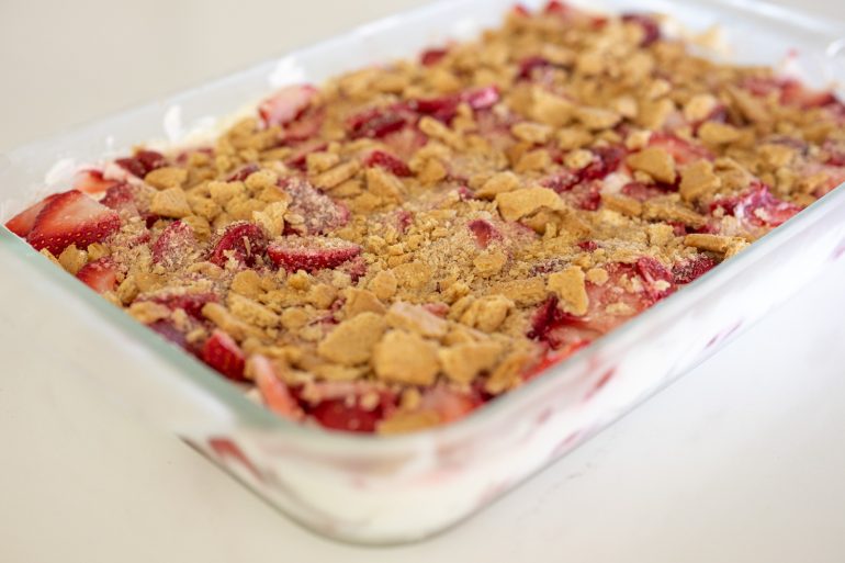 A glass baking dish with filled with a strawberry dessert topped with graham cracker crumbs.